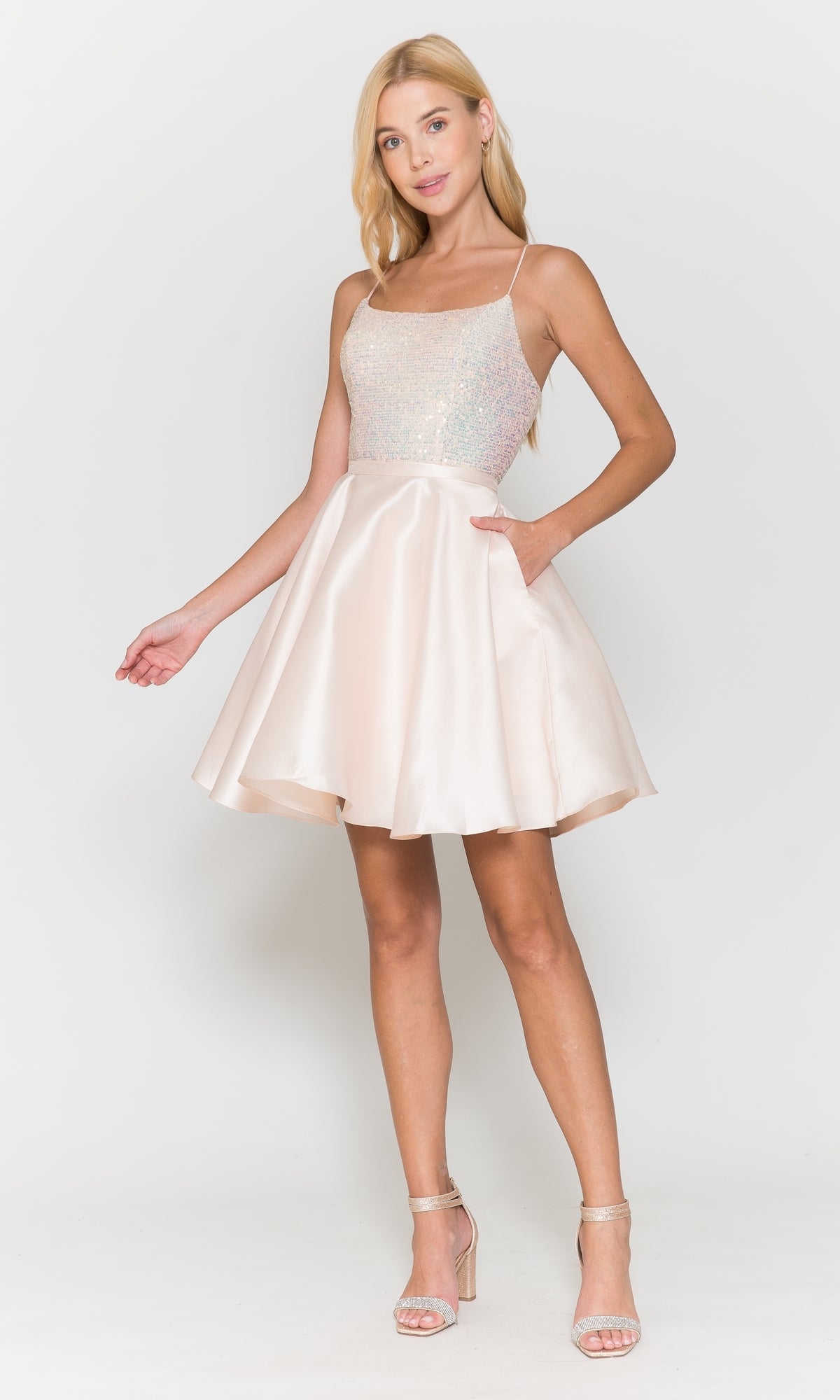 A woman models the Sequin-Bodice Short Flared Homecoming Dress 8730—sleeveless, light pink, with a sparkly bodice and a chic A-line skirt—standing in heels against a white background. Ideal for special events.